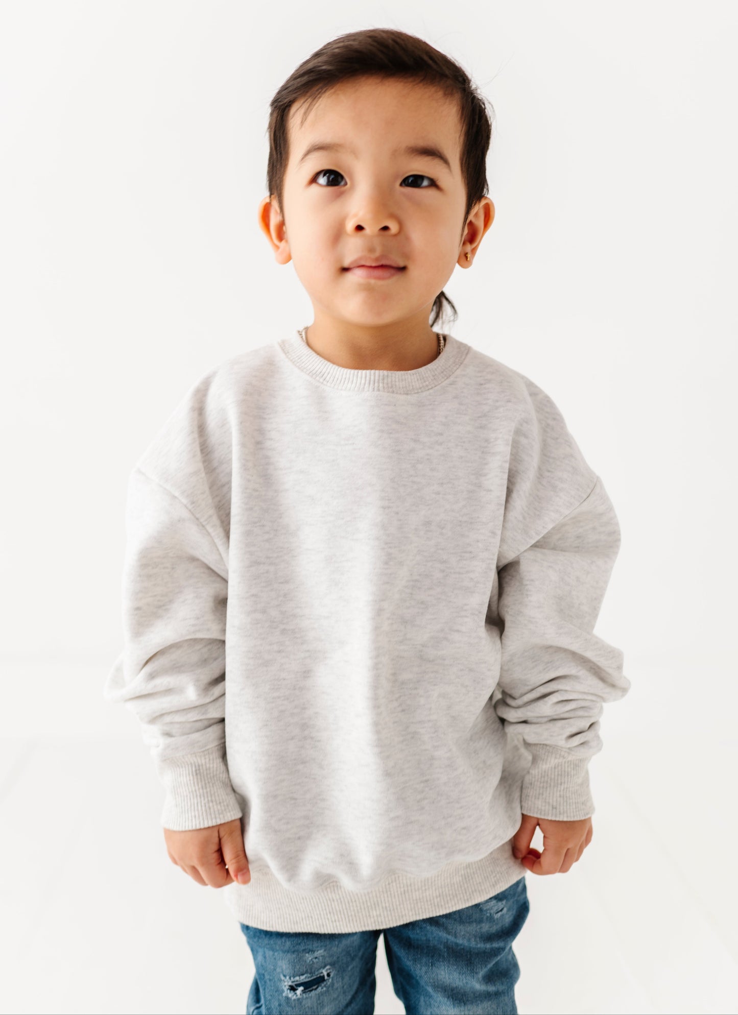 Young boy wearing a gray sweatshirt and blue jeans on a white background