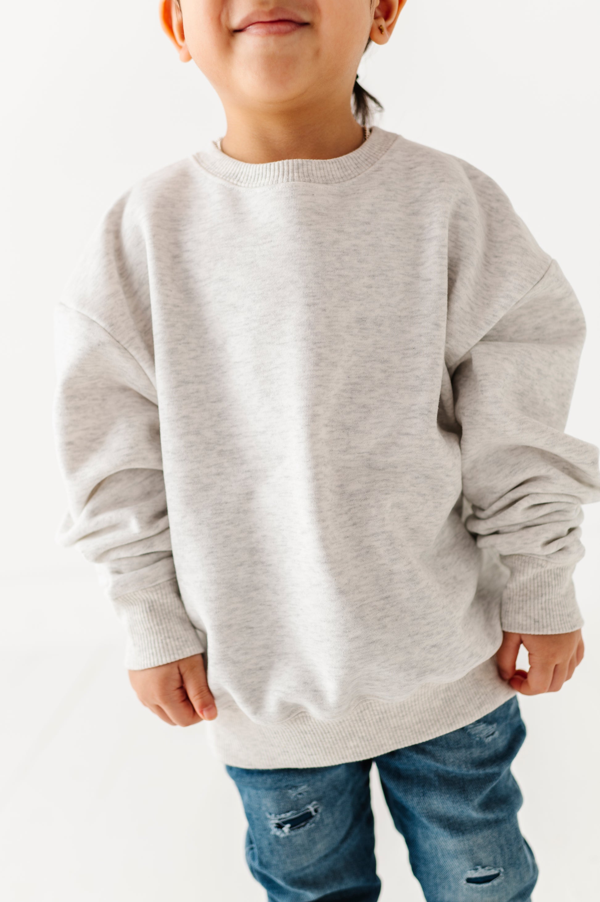 Child wearing a gray sweatshirt and blue jeans on a white background