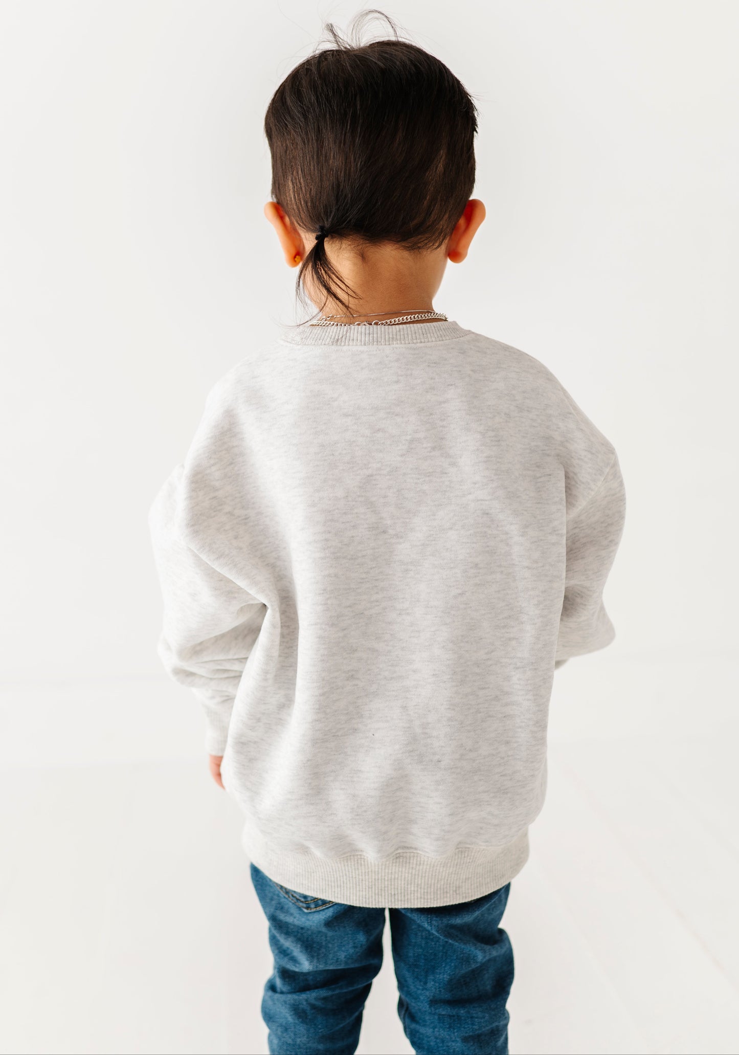 Child wearing a light gray sweater and blue jeans on a white background