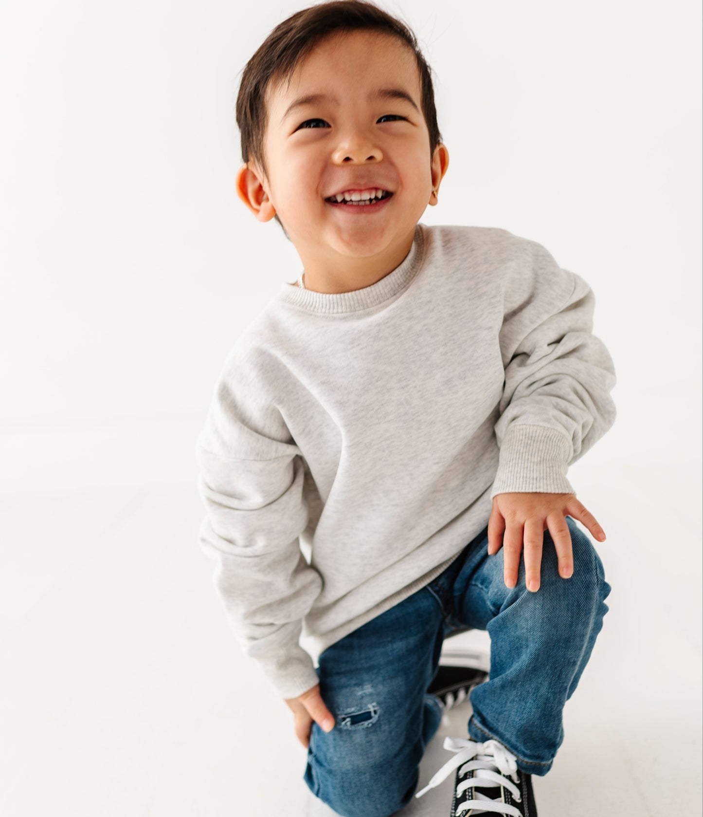 Child wearing a gray sweater and blue jeans with black sneakers on a white background